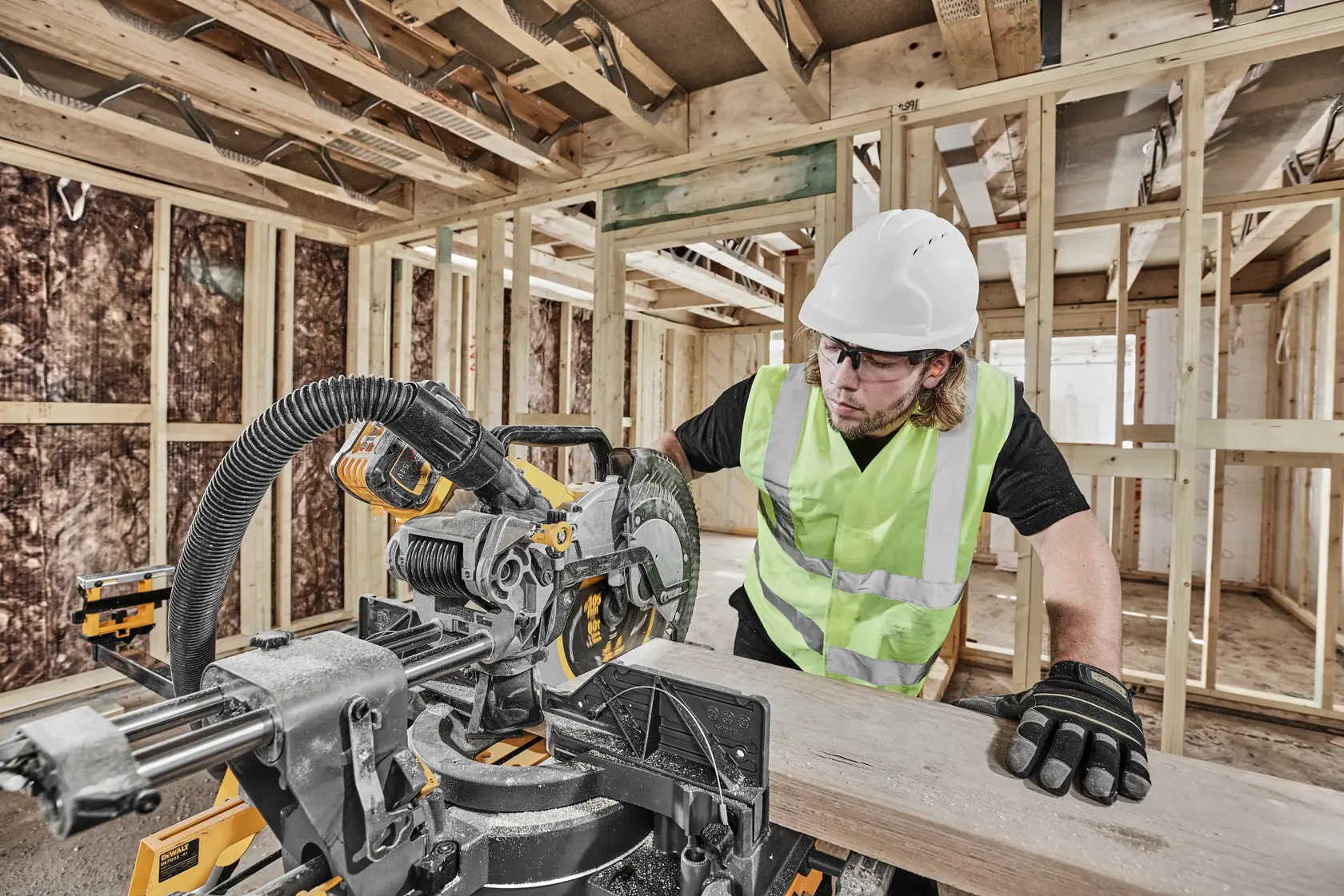 Arbeiter nutzt DEWALT DCS781N Kappsäge für Holz, Baustelle, trägt Sicherheitsausrüstung.