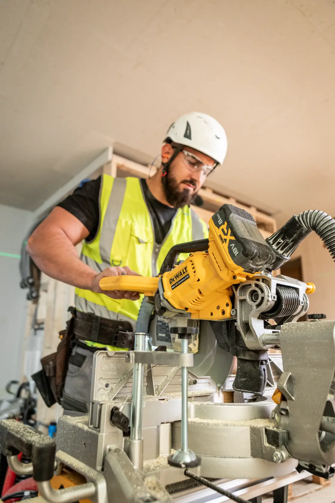 Worker uses yellow DEWALT DCS782N saw on construction site, wearing high-visibility vest and helmet.