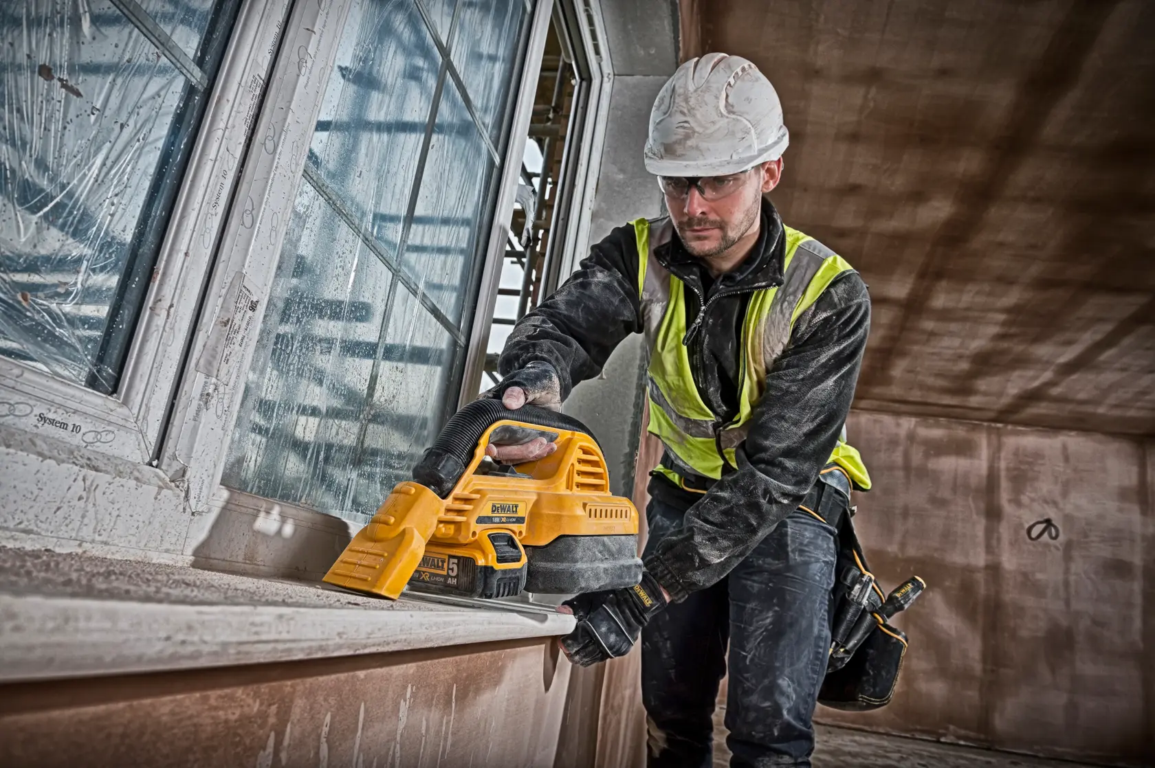 Trabajador usa aspiradora portátil DEWALT DCV517N en alféizar. Equipamiento de seguridad.