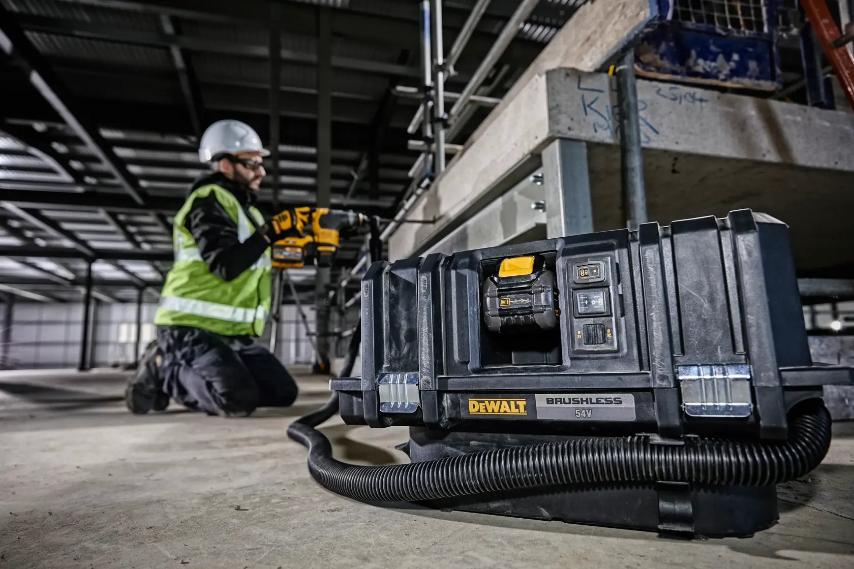 Aspirador DEWALT DCV586MT2 en suelo de obra, trabajador arrodillado cerca con equipo de seguridad.