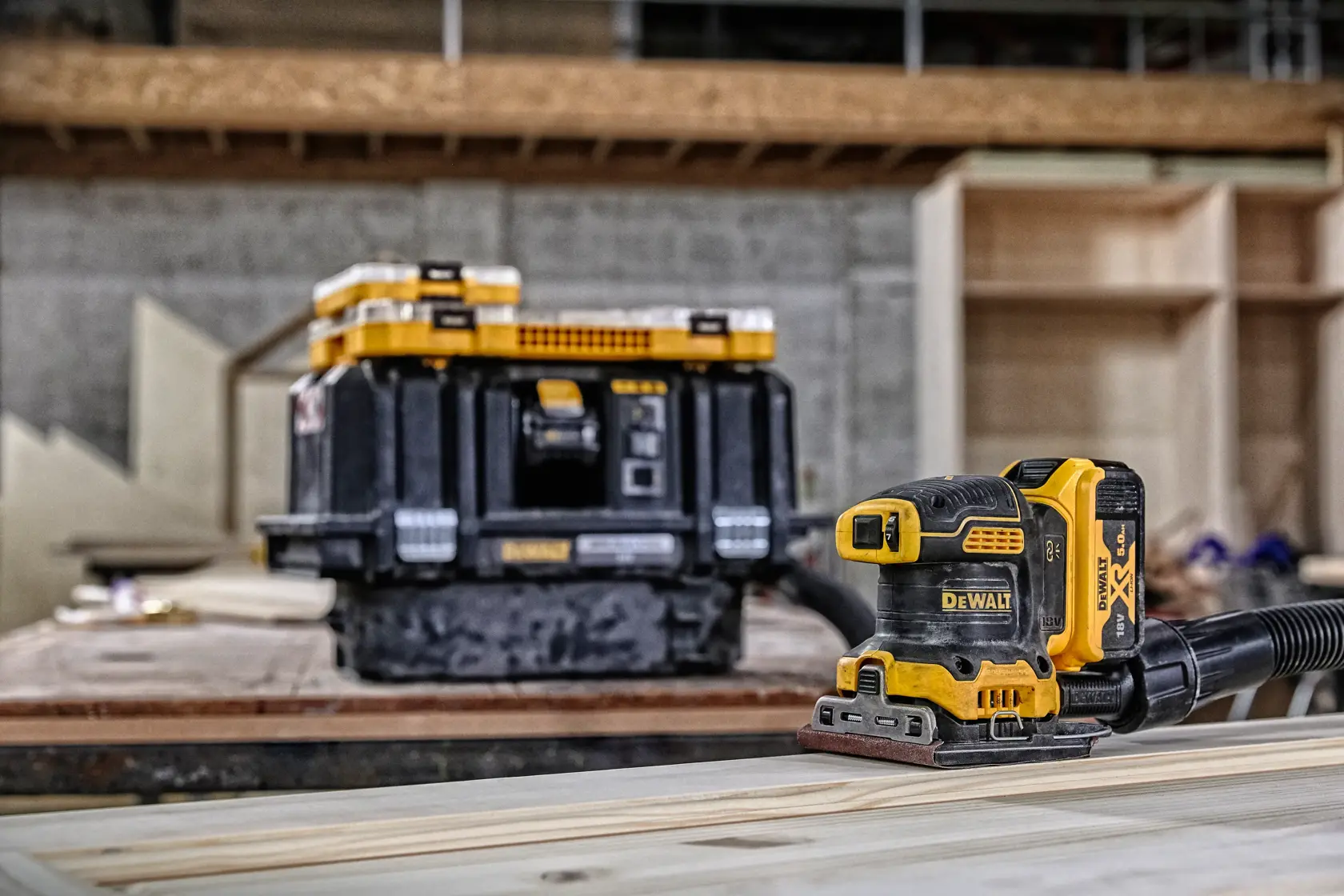DEWALT DCW200N cordless sander and tool case on a wooden workspace in a workshop.