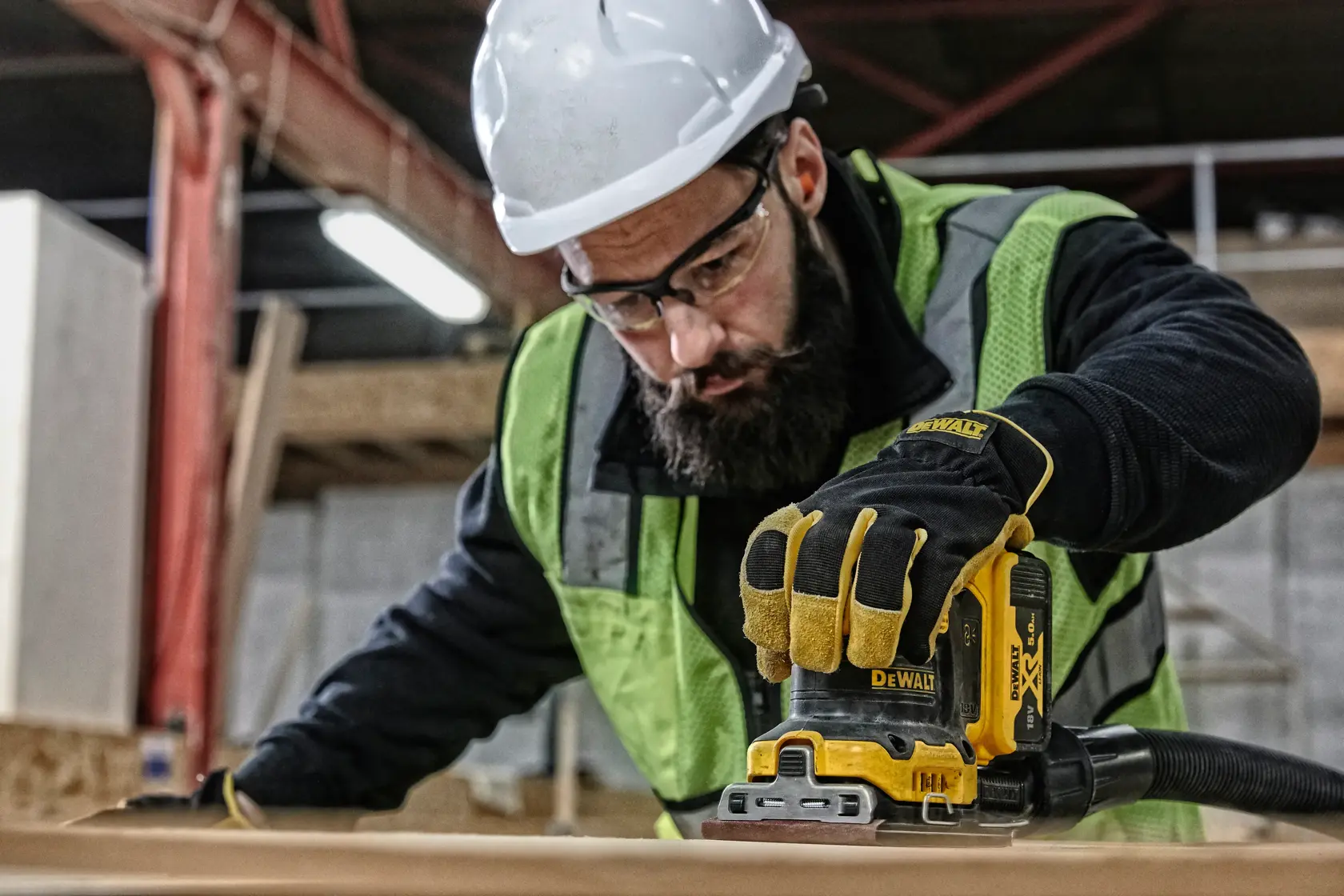 Trabajador usa DEWALT DCW200P2 alisar madera, con guantes, casco y chaleco en obra.