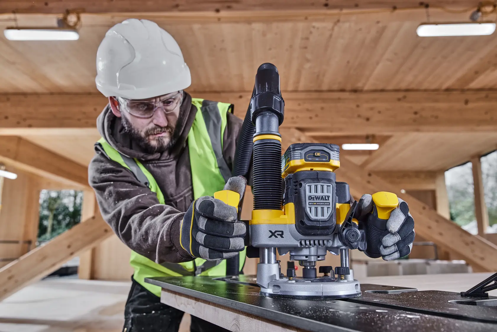 Arbeiter verwendet DEWALT DCW620H2 Akku-Fräse auf Holz, mit Schutzkleidung auf Baustelle.