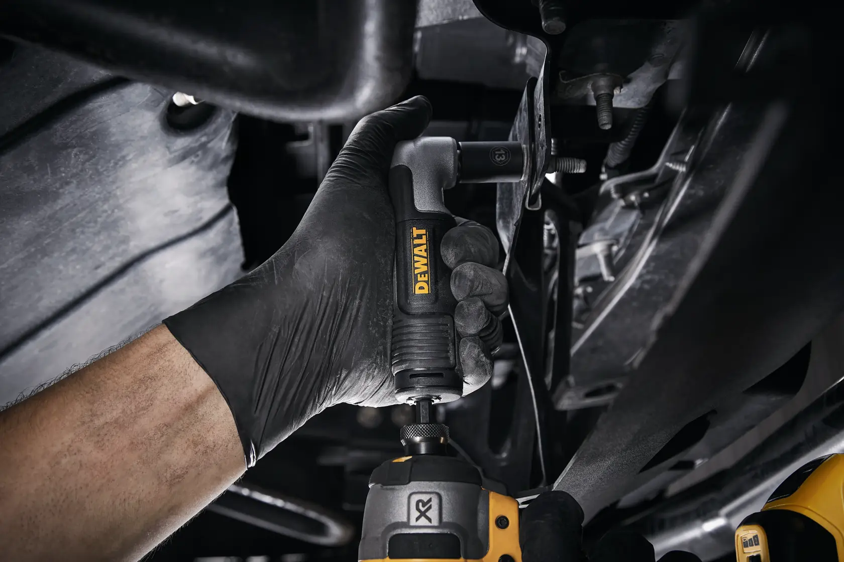 Mano con accesorio angular DEWALT bajo un vehículo para taladrar o fijar en espacios reducidos.