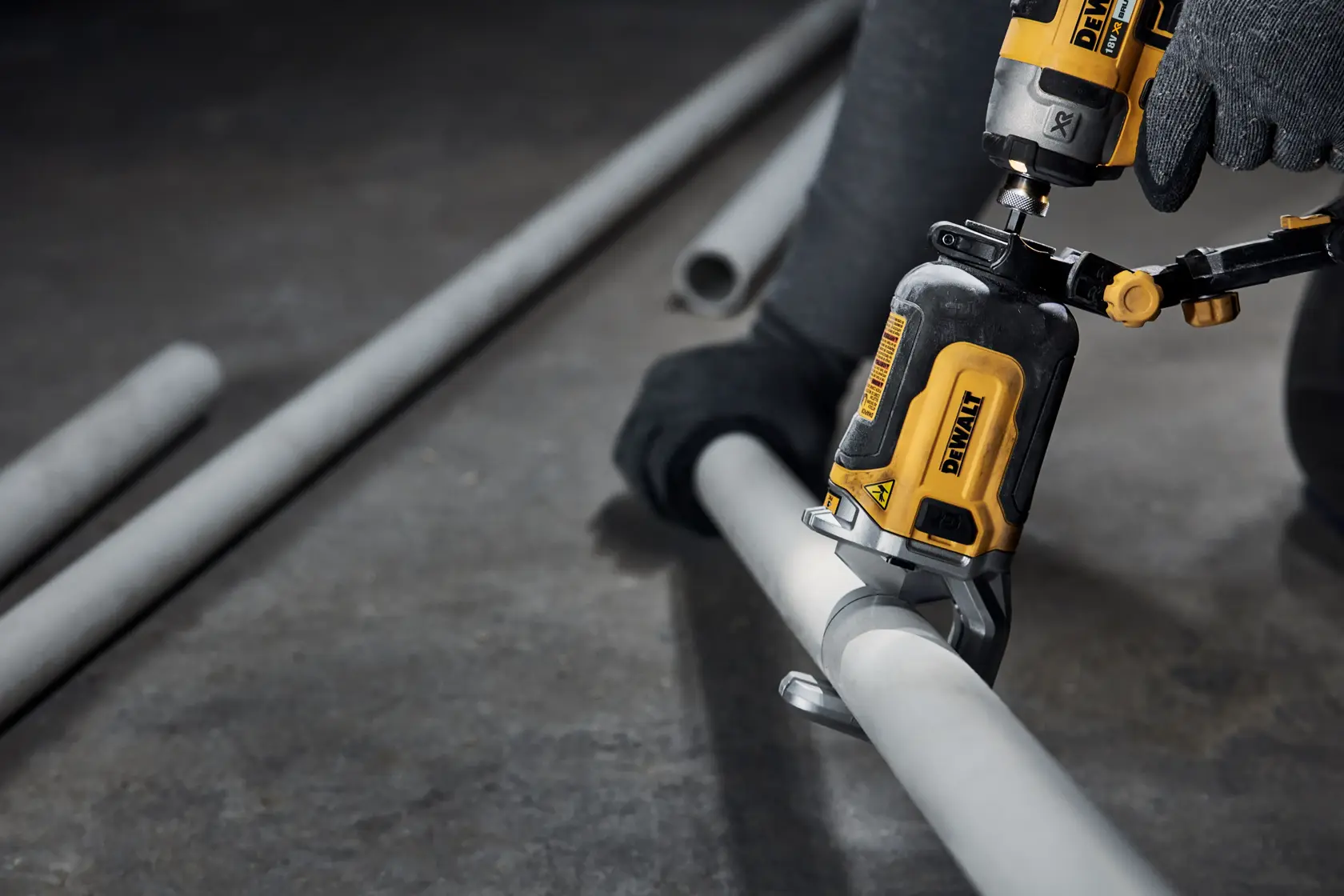 Nærbilde av et DEWALT elektrisk verktøy brukt av en person med hansker for å kutte et grått metallrør på verkstedsgulvet.