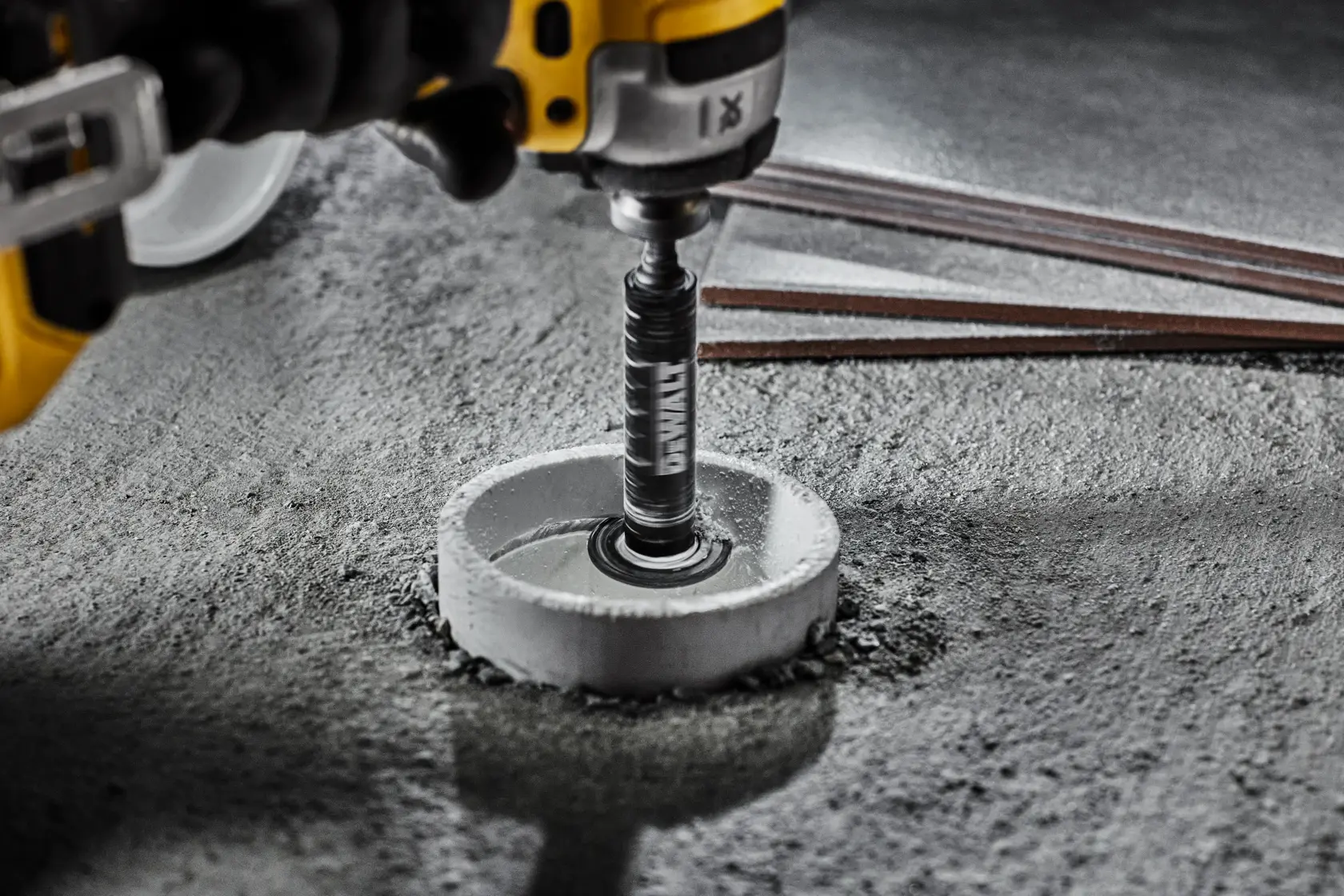 DEWALT drill with hole saw attachment cutting into concrete surface, metal rods visible nearby.