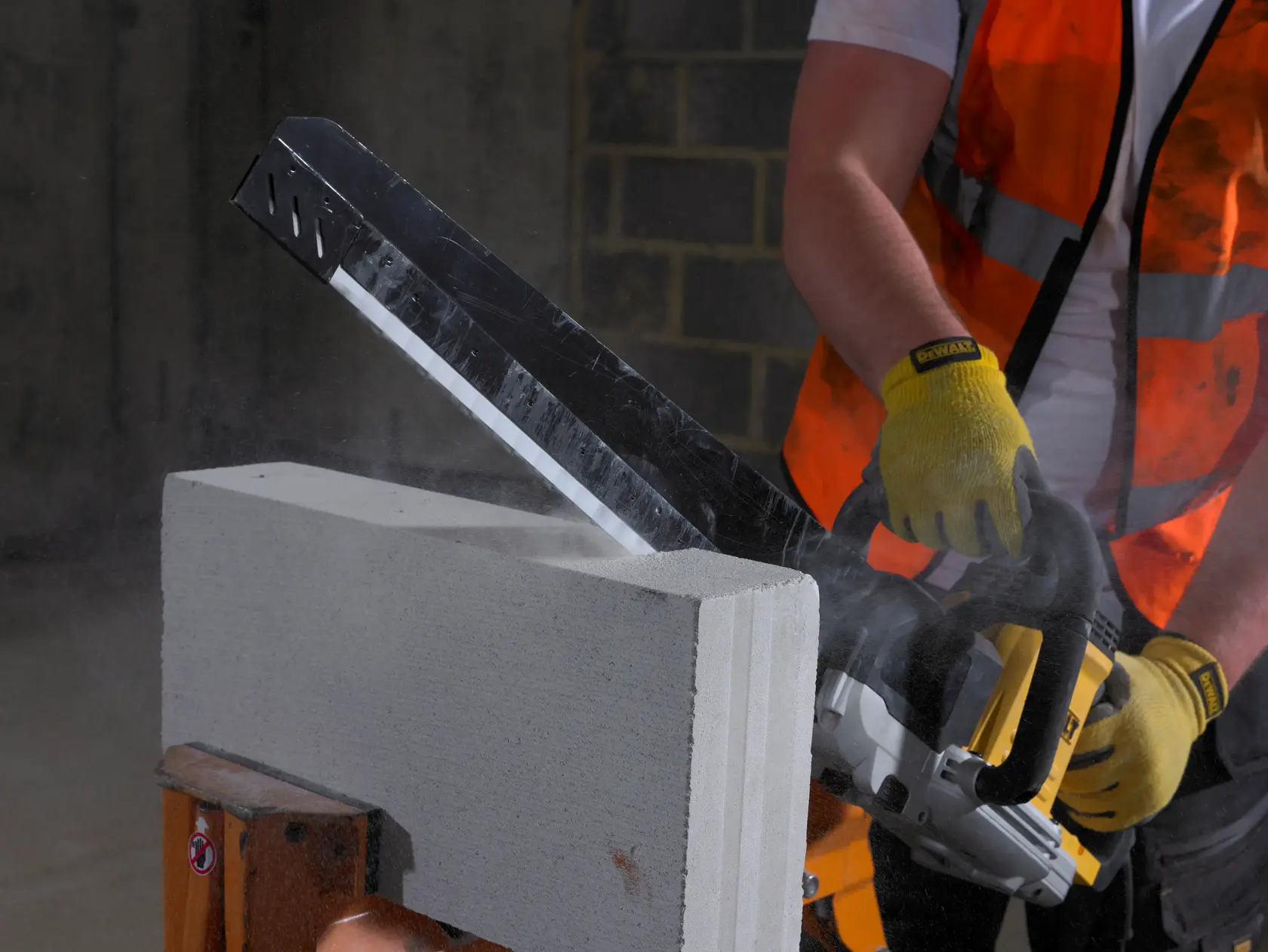 Trabajador corta bloque de hormigón con sierra DEWALT, usando guantes y chaleco.