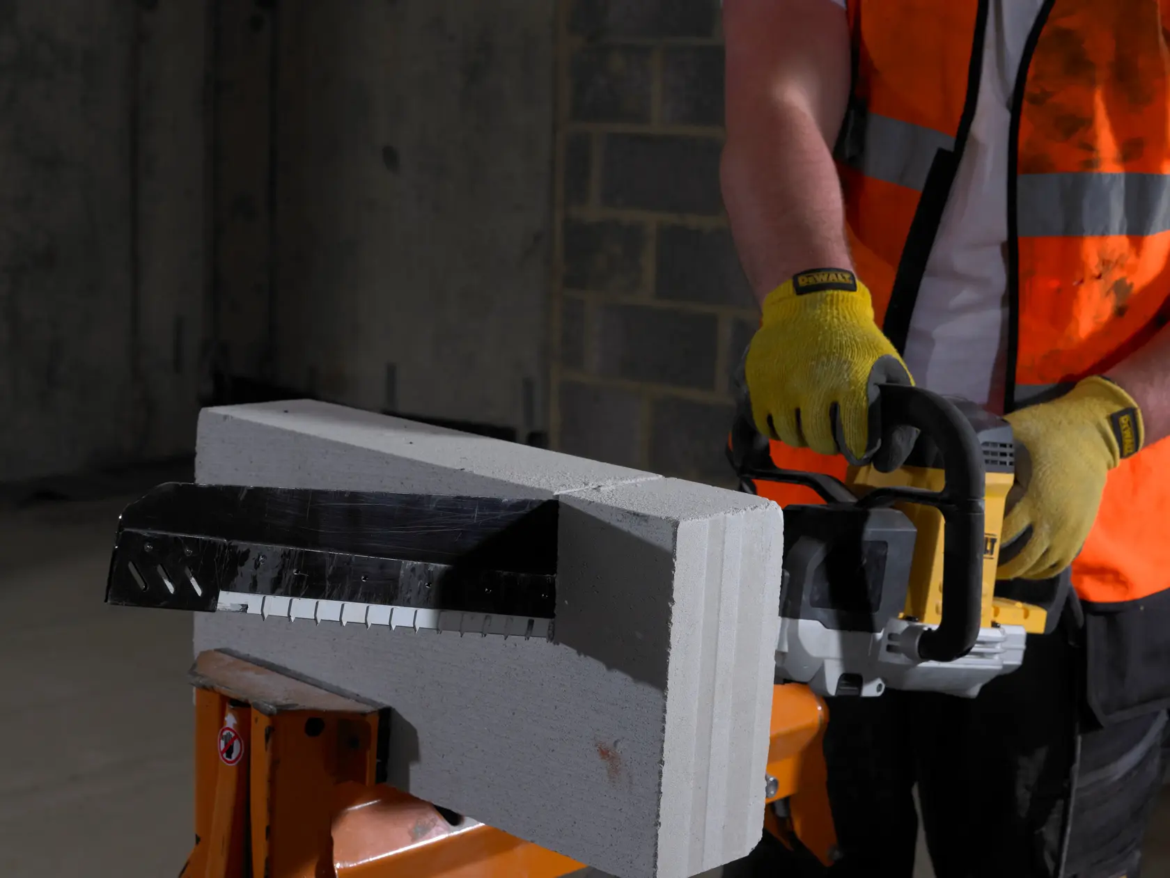 Persona usa una sierra DEWALT y guantes para cortar un bloque de concreto en interior.