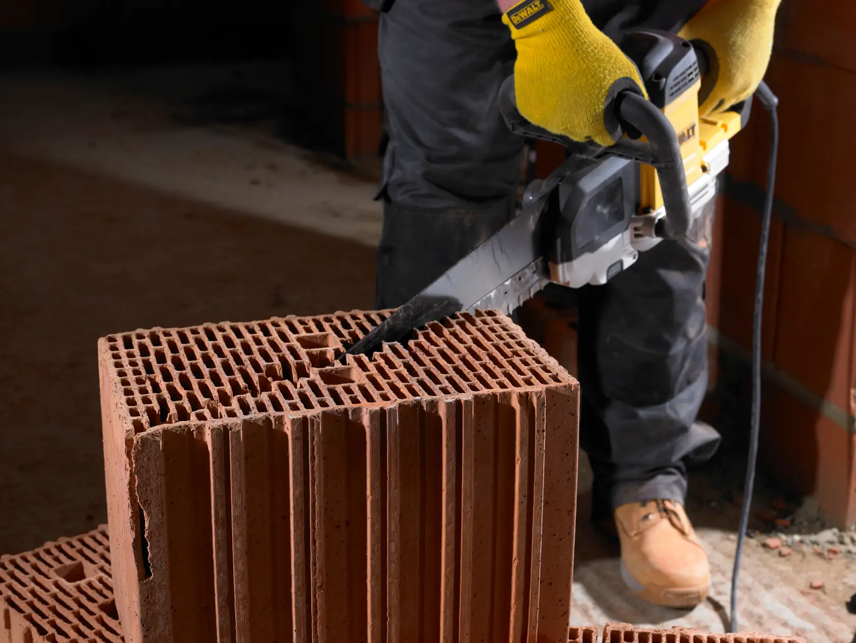 Persona corta un gran bloque de ladrillo hueco con una sierra eléctrica DEWALT en construcción.