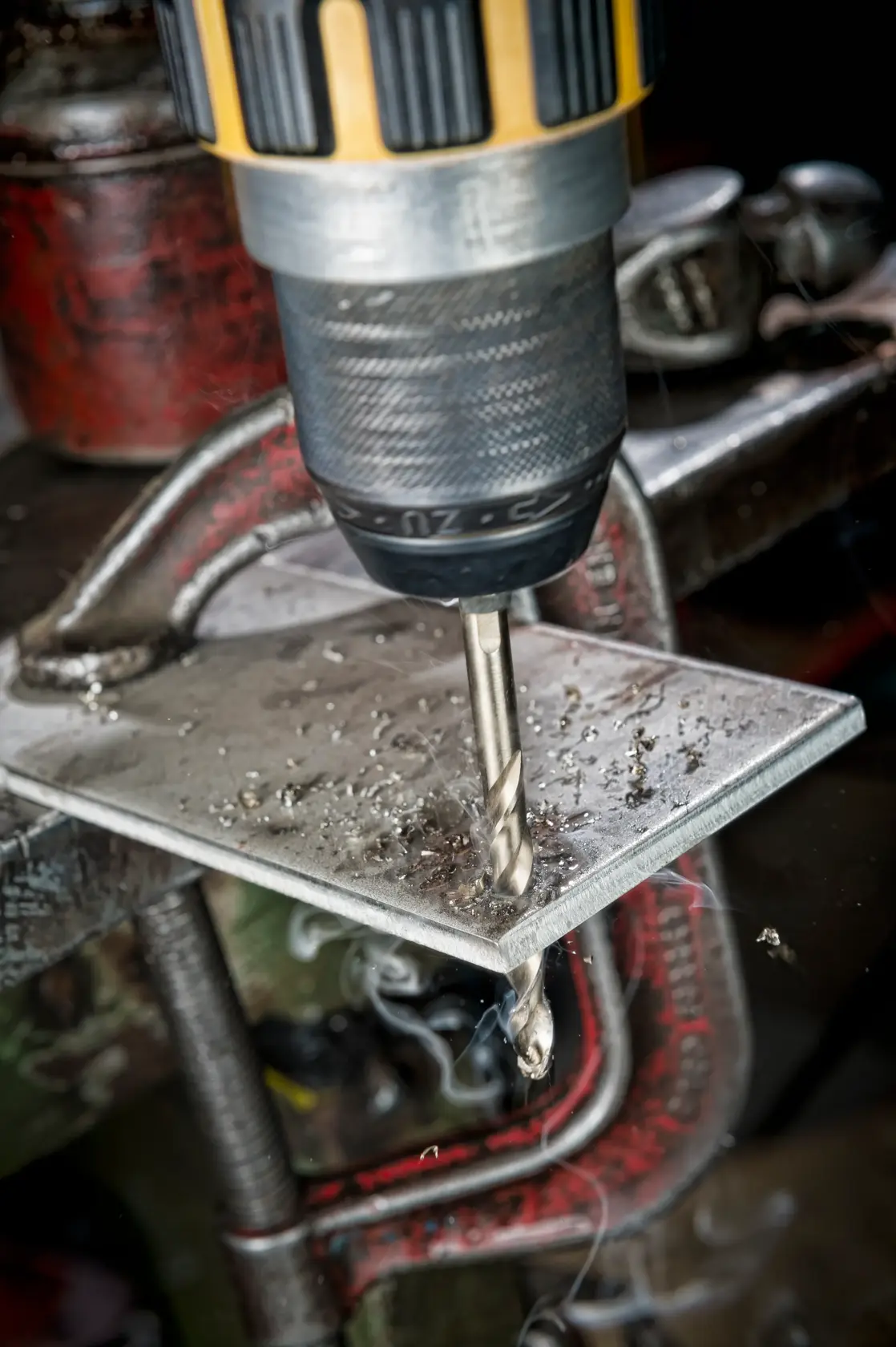 DEWALT drill bit DT4963 drilling through metal sheet held by a clamp, with metal shavings visible.