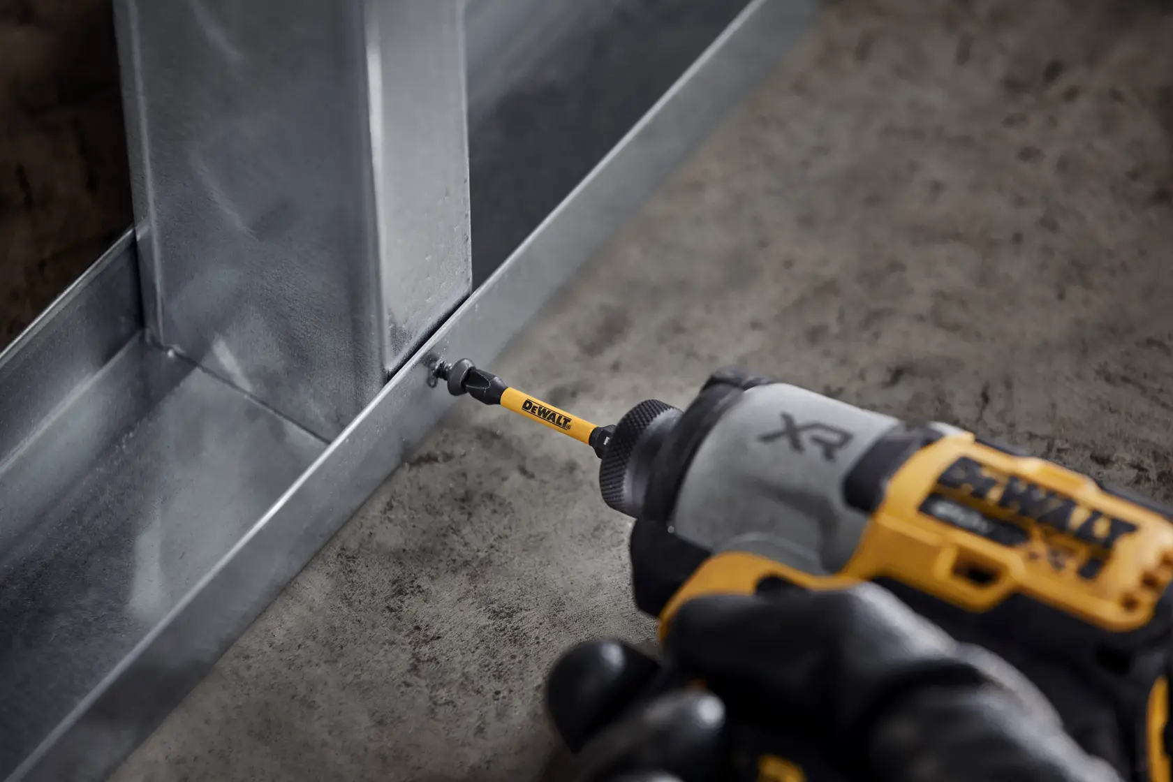 Taladro DEWALT atornilla en un marco metálico sobre el suelo de una obra.
