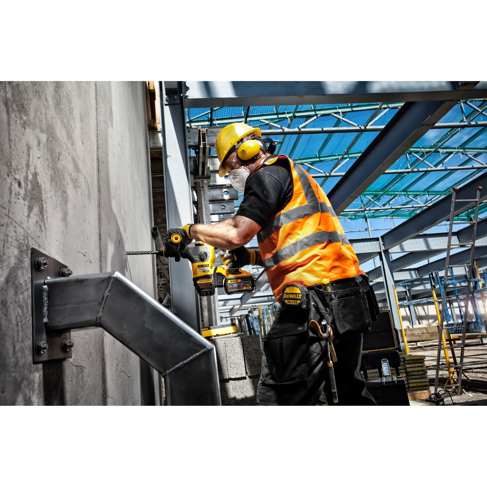 Worker uses a DEWALT drill on a concrete wall at a construction site, wearing safety gear and high-visibility vest.