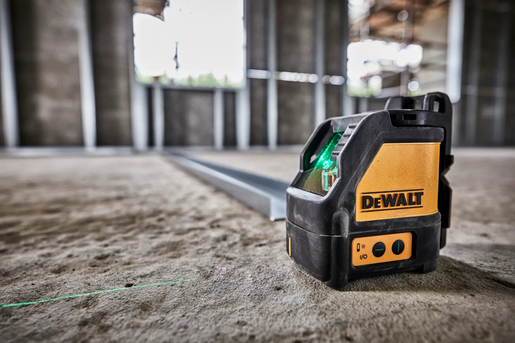 A DeWalt laser level tool projecting a green laser line across a concrete floor in an unfinished building with exposed metal framing.