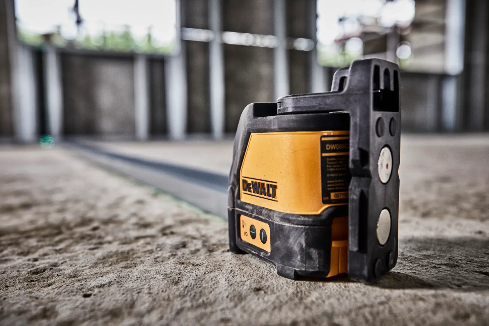 A DeWALT laser level tool placed on the floor inside an unfinished building, projecting a green laser line across the ground for construction alignment.